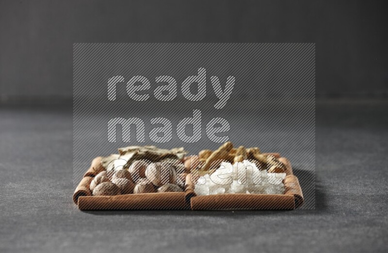 4 مربعات من عيدان القرفة ممتلئة بأوراق الغار والملح الأبيض وأصابع الكركم وجوزة الطيب على أرضية سوداء