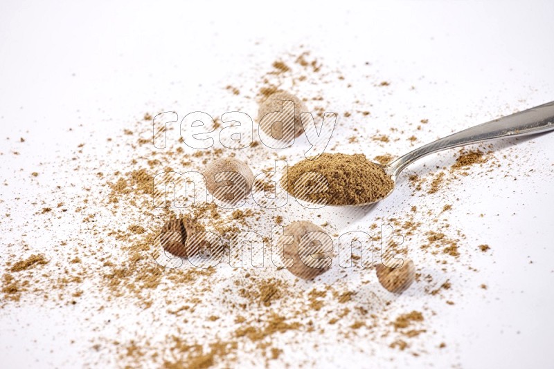 A metal spoon full of nutmeg powder with nutmeg powder and seeds beside it on a white flooring in different angles