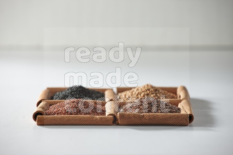 4 مربعات من أعواد القرفة ممتلئة بحبة البركة وبذور الخردل وبذور الكتان وحب الرشاد على أرضية بيضاء