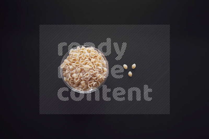 Shells pasta in a glass bowl on black background