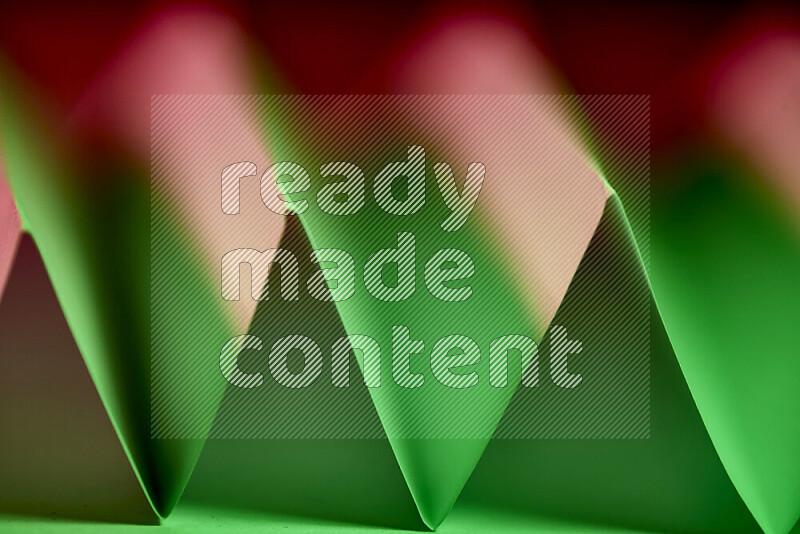 A close-up abstract image showing sharp geometric paper folds in green and red gradients