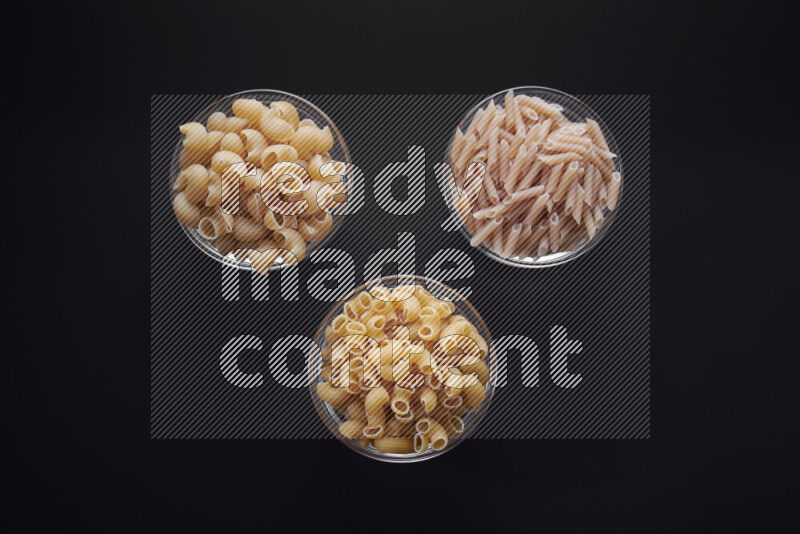 Different pasta types in glass bowls on black background