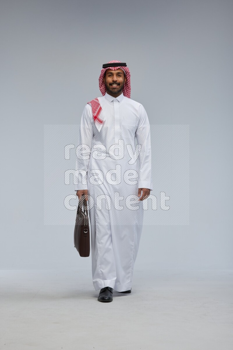 Saudi man Wearing Thob and shomag standing holding bag on Gray background