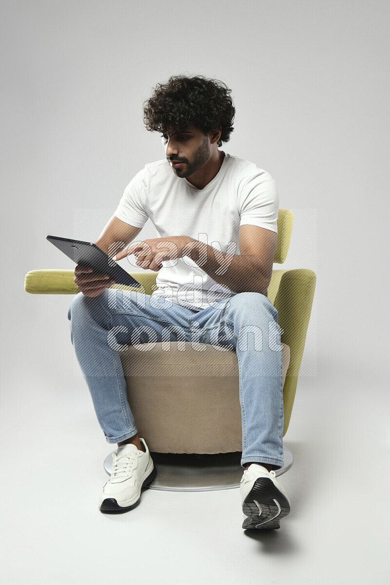 A man wearing casual sitting on a chair browsing on a tablet on white background