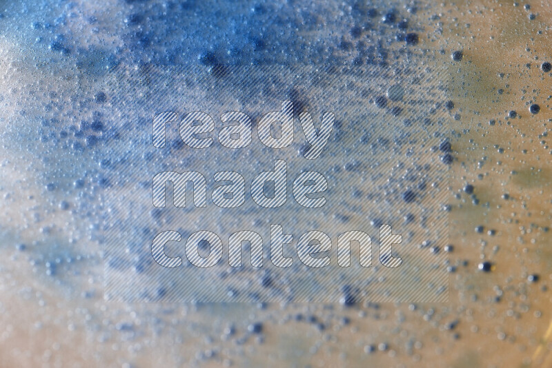 لقطات مقربة لقطرات ألوان مائية زرقاء على سطح الزيت على خلفية صفراء