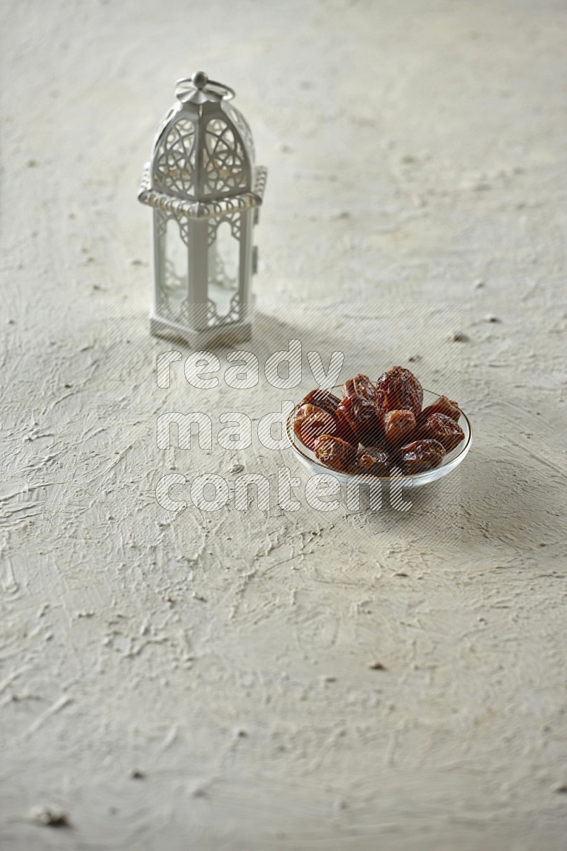 A white lantern with drinks, dates, nuts, prayer beads and quran on textured white background