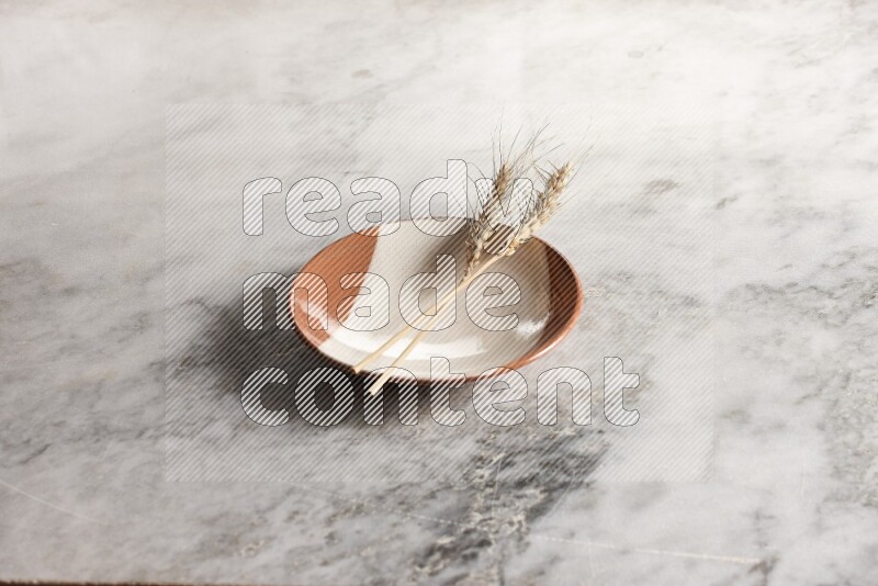 Wheat stalks on multicolored pottery plate on grey marble background