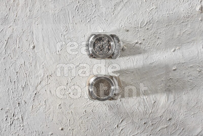 حبات ومسحوق الفلفل الأسود في أوعية زجاجية علي خلفية بيضاء