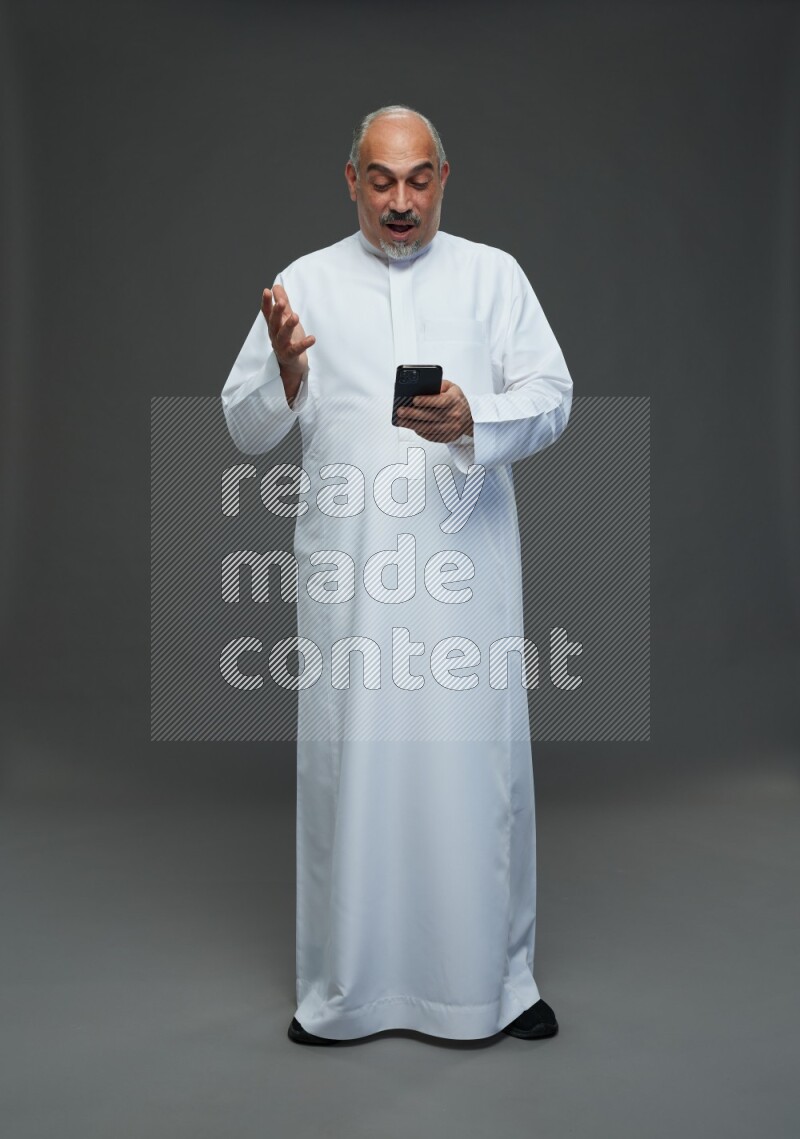 Saudi man without shomag Standing texting on phone on gray background