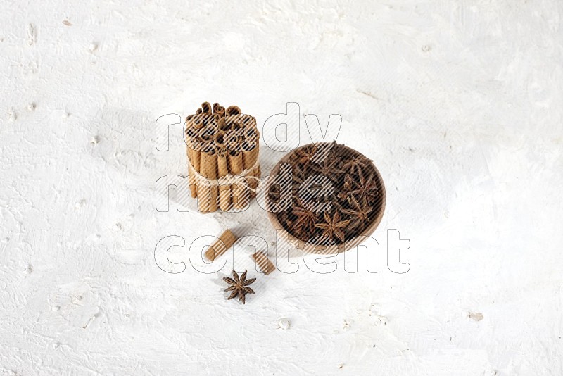 A stacked and bounded cinnamon sticks and a wooden bowl full of star anise on a white background