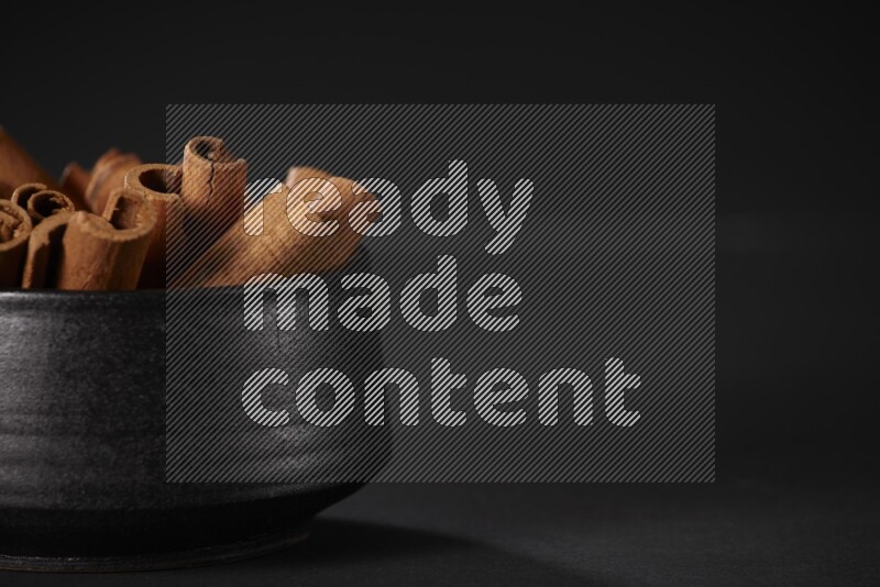 Cinnamon sticks in a black bowl on a black background in different angles