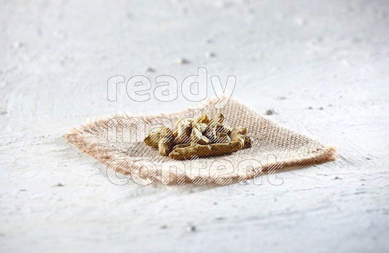 Dried turmeric whole fingers on a piece of burlap on a textured while flooring