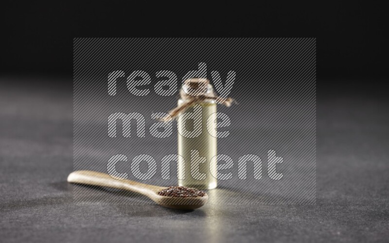 وعاء خشبي ممتلئ بحبوب بذر الكتان مع زجاجة من زيت بذر الكتان علي خلفية سوداء