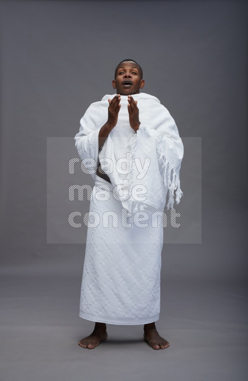 A man wearing Ehram standing showing how to sneeze on gray background