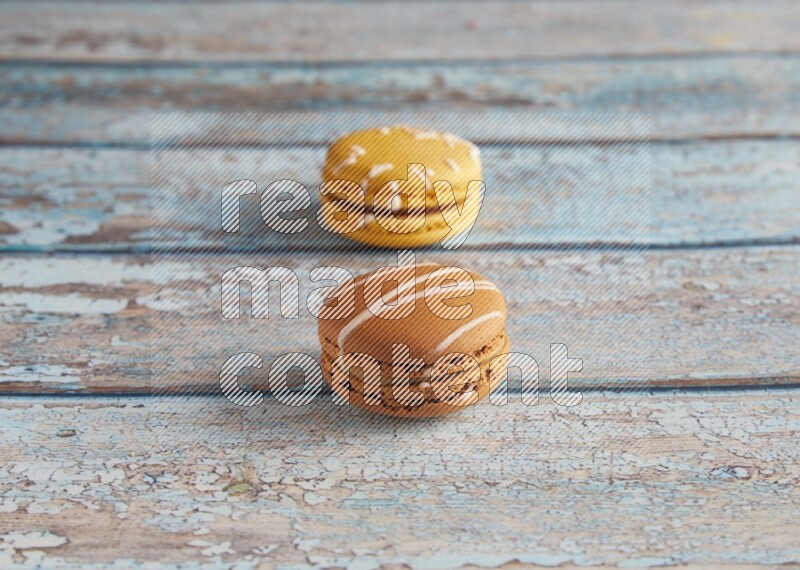 45º Shot of of two assorted Brown Irish Cream, and Yellow Piña Colada macarons on light blue background