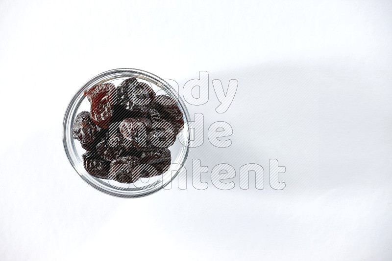 A glass bowl full of dried plums on a white background in different angles