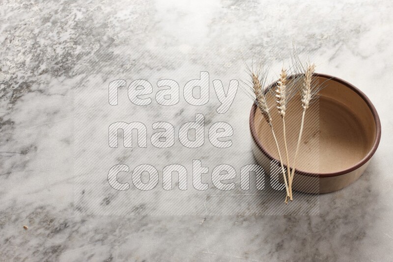 Wheat stalks on beige pottery oven bowl on grey marble background