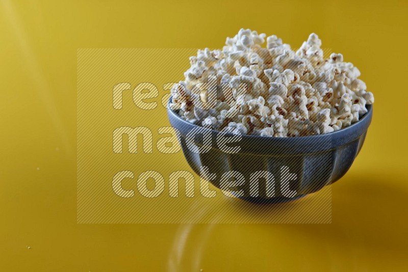 A blue pottery bowl full of popcorn on a yellow background in different angles