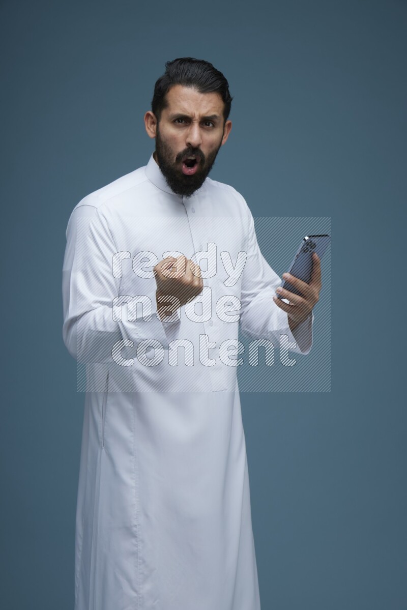 A man Texting in a blue background wearing Saudi Thob