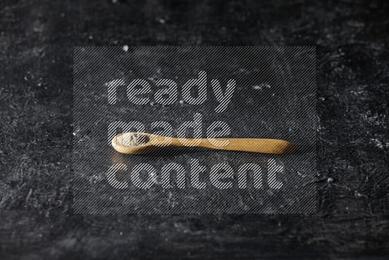 ملعقة خشبية مليئة ببودرة الفلفل الأبيض على أرضية سوداء