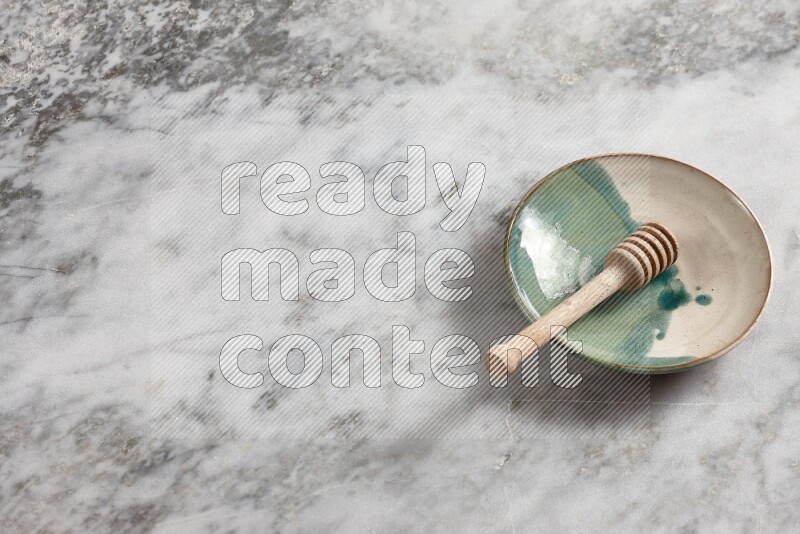 Multicolored pottery plate with wooden honey dipper in it on grey marble background