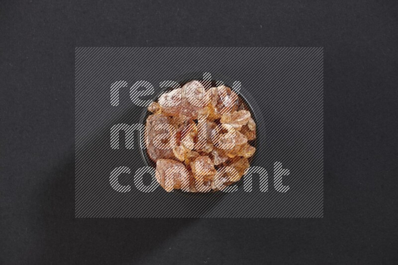 وعاء فخاري أسود ممتلئ بقطع الصمغ العربي علي خلفية سوداء