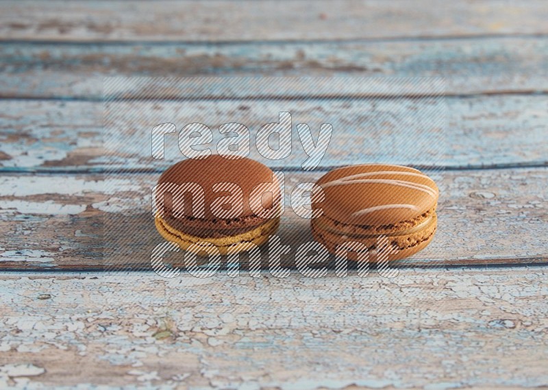 45º Shot of of two assorted Brown Irish Cream, and Yellow, and Brown Chai Latte macarons  on light blue background