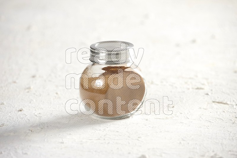 Herbs glass jar full of cinnamon powder on a textured white background