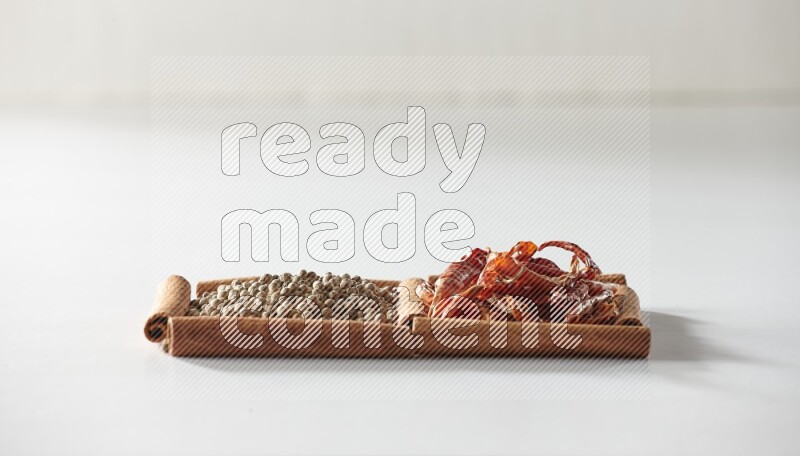 مربعان من أعواد القرفة ممتلئان بالفلفل الحار المجفف وحبوب الفلفل الأبيض علي خلفية بيضاء