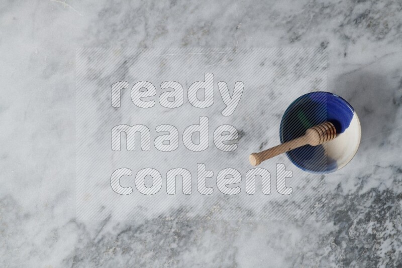 Multicolored pottery bowl with wooden honey dipper in it on grey marble background