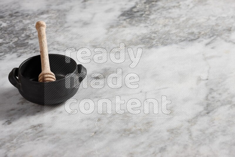 Black pottery bowl with wooden honey dipper in it on grey marble background