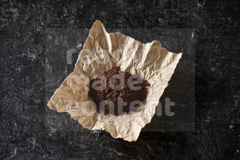 Cloves powder in crumpled piece of paper on a textured black flooring