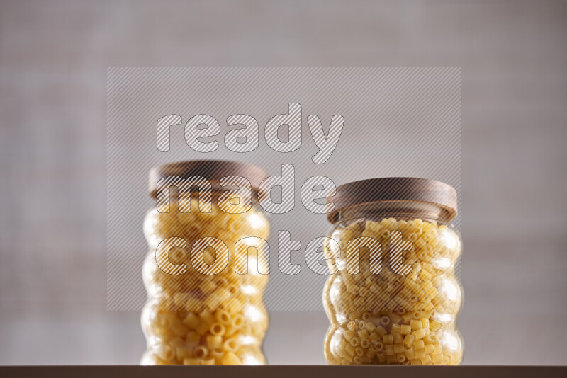 Raw pasta in glass jars on beige background