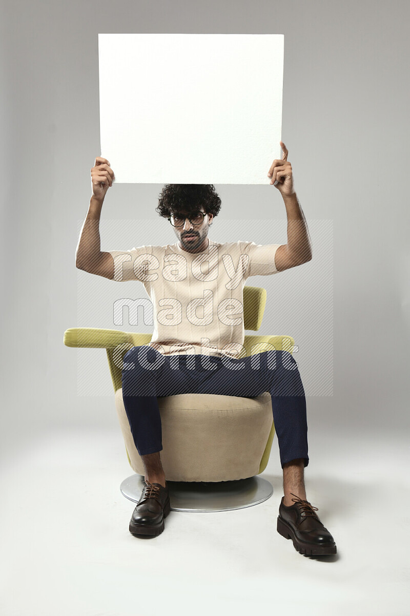 A man wearing casual sitting on a chair holding a white board on white background