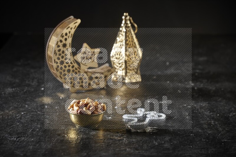 Nuts in a metal bowl with prayer beads beside golden lanterns in a dark setup
