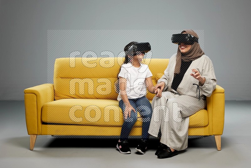 A girl and her mother sitting playing with VR on gray background