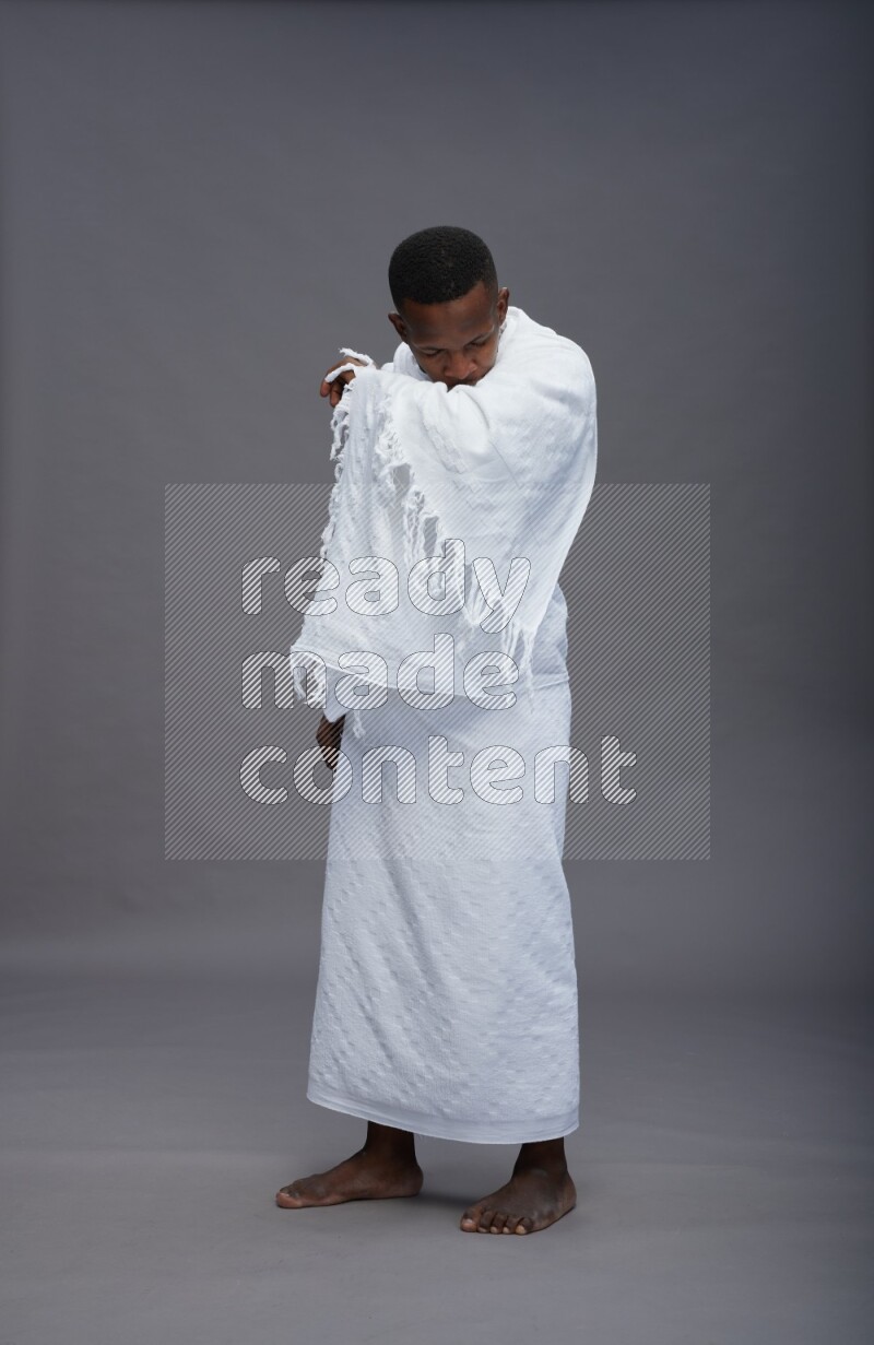 A man wearing Ehram standing showing how to sneeze on gray background