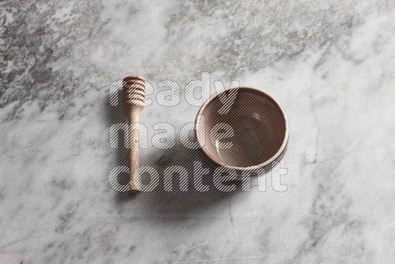 Multicolored pottery bowl with wooden honey dipper on the side on grey marble background