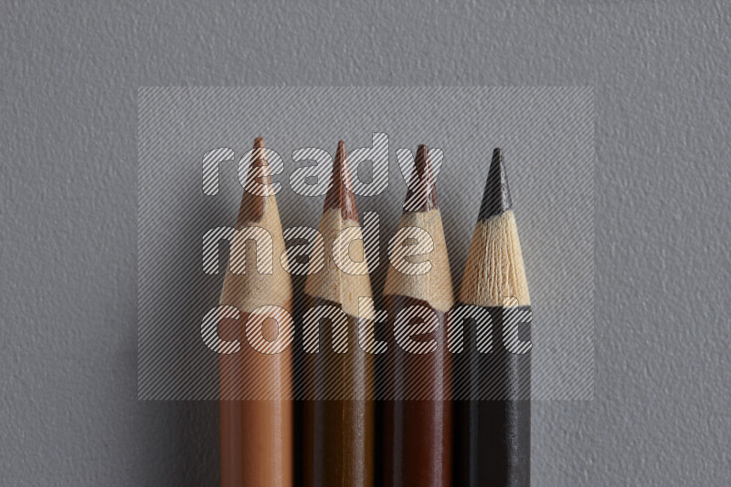 A collection of colored pencils arranged showcasing a gradient of brown hues on grey background