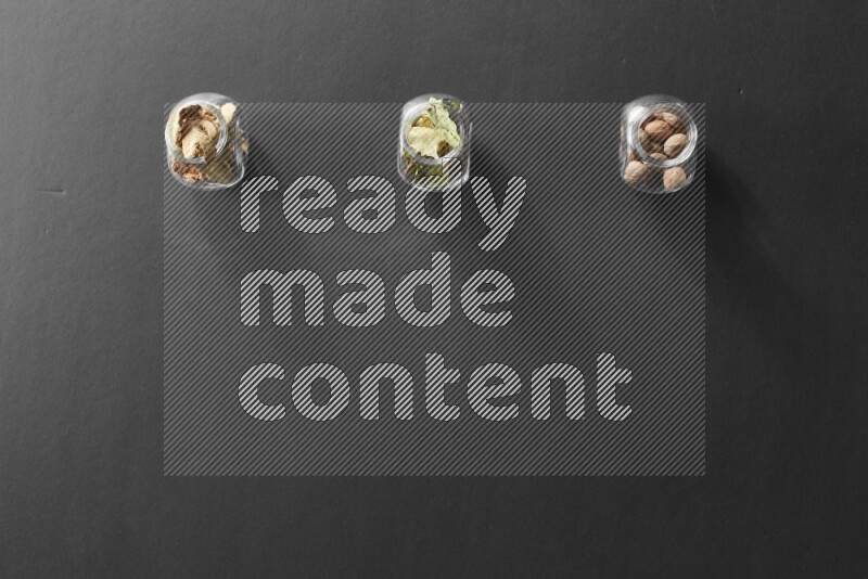 3 glass spice jars full of laurel bay leaves, ginger and nutmeg on black flooring