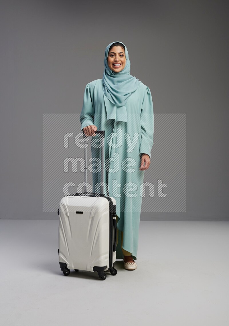 Saudi Woman wearing Abaya standing holding Travel bag on Gray background