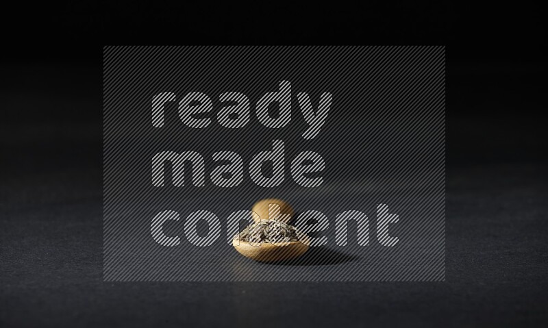 ملعقة خشبية ممتلئة بحبوب الكمون على خلفية سوداء