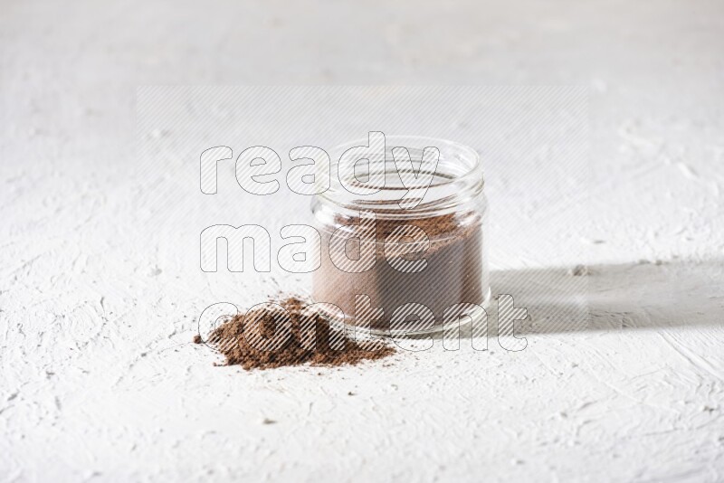 A glass jar full of cloves powder on a textured white flooring