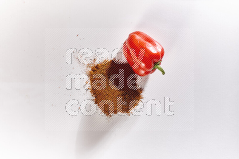 A bunch of ground paprika powder with a red bell pepper beside it on white background