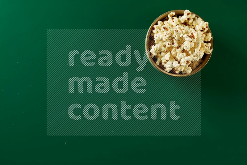 An off white ceramic bowl full of popcorn on a green background in a top view shot