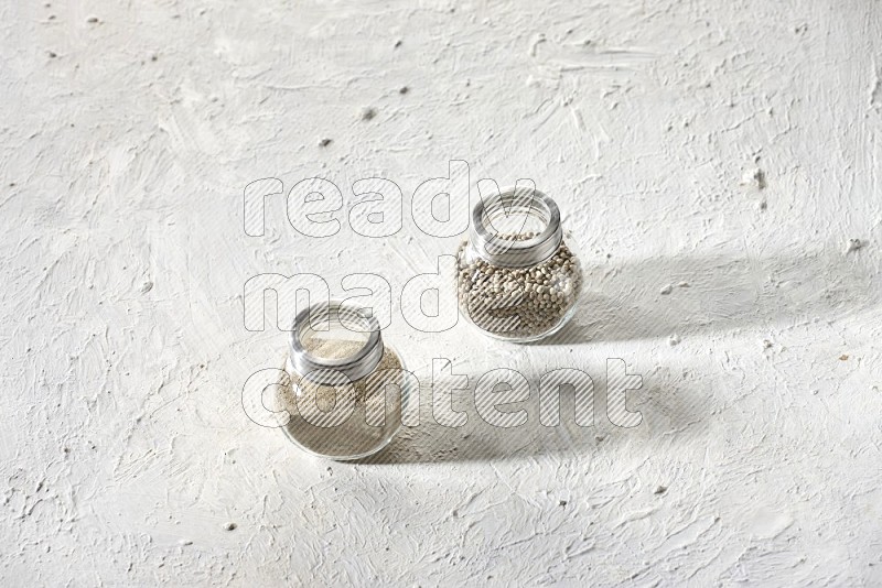 وعاءين زجاجيين عشبيين ممتلئين بحبوب وبودرة الفلفل الأبيض على أرضية بيضاء