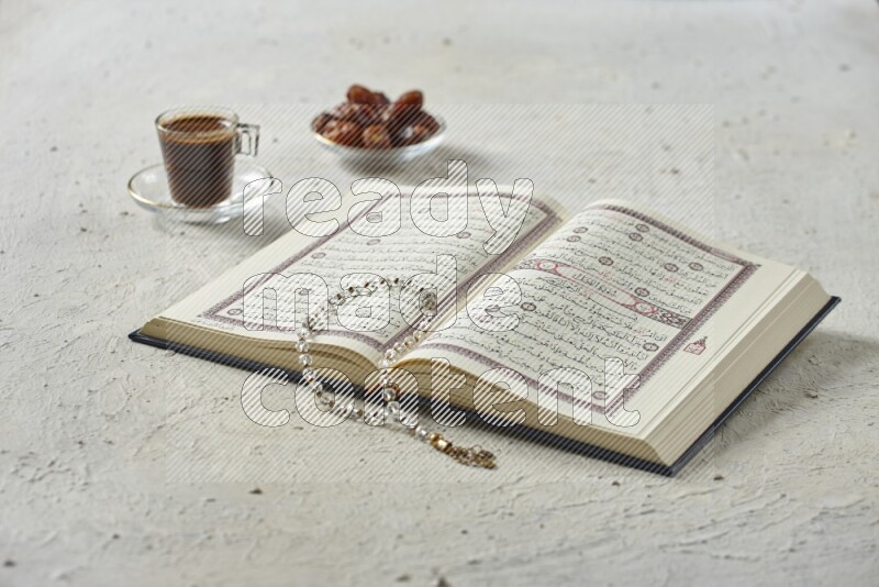 Quran with dates, prayer beads and different drinks all placed on textured white background