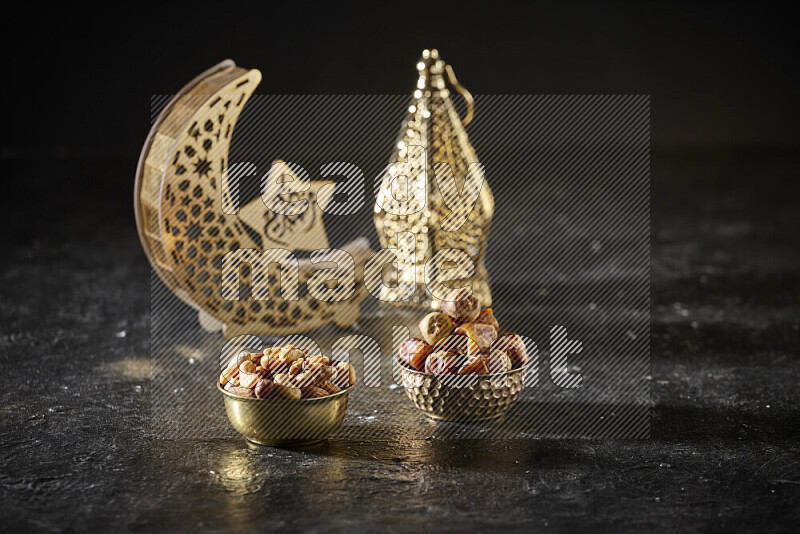 Dates in a metal bowl with mixed nuts beside golden lanterns in a dark setup