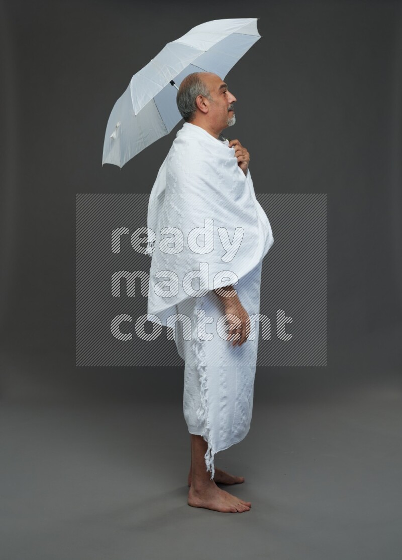 A man wearing Ehram Standing holding umbrella on gray background