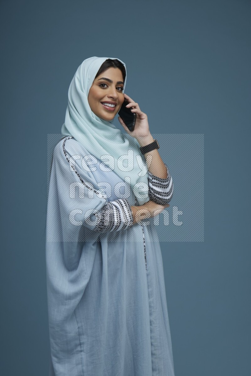 A Saudi woman having a Call in a blue background wearing blue Abaya with hijab